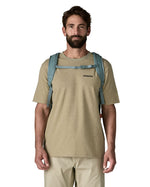 Man wearing Patagonia's refugio 32L daypack in sage blue. Shows shows front buckle fastened