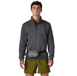A man wearing the Patagonia terravia mini bum bag in noble grey available at Babipur around the waist showing the zipped compartment on the front panel