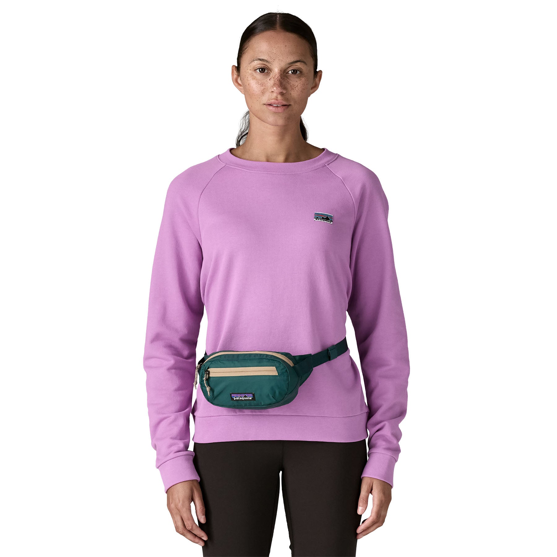 A woman wearing the Patagonia terravia mini bum bag in cascade green available at Babipur around the waist showing the zipped compartment on the front panel