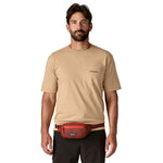 A man wearing the Patagonia terravia mini bum bag in dried vanilla available at Babipur around the waist showing the zipped compartment on the front panel