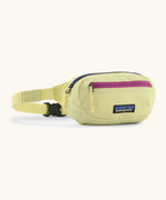 Patagonia 100% recycled nylon weather resistant terravia mini hip pack in pale yellow. Features 2 compartments with navy and pink zip detail