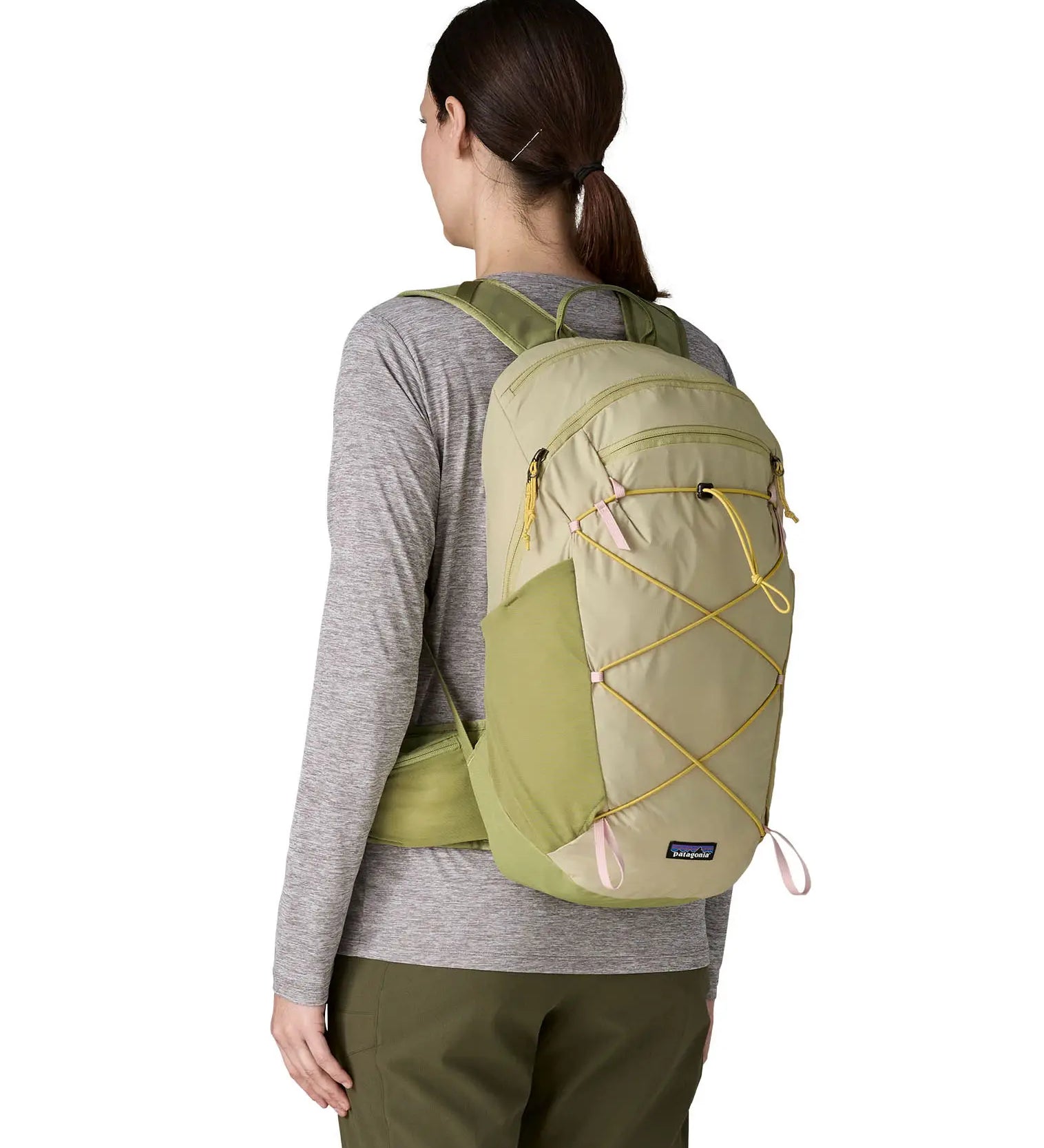 Woman wearing Patagonia's terravia 22L backpack in light green on the back with dark yellow gear elastics and mesh side pockets