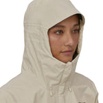 A person is wearing the Patagonia Women's Torrentshell 3L Rain Jacket and has the jacket fully zipped up with the hood up. The image is showing the coat zips all the way up to the chin and the hood comes quite far down to protect the face and neck from rain