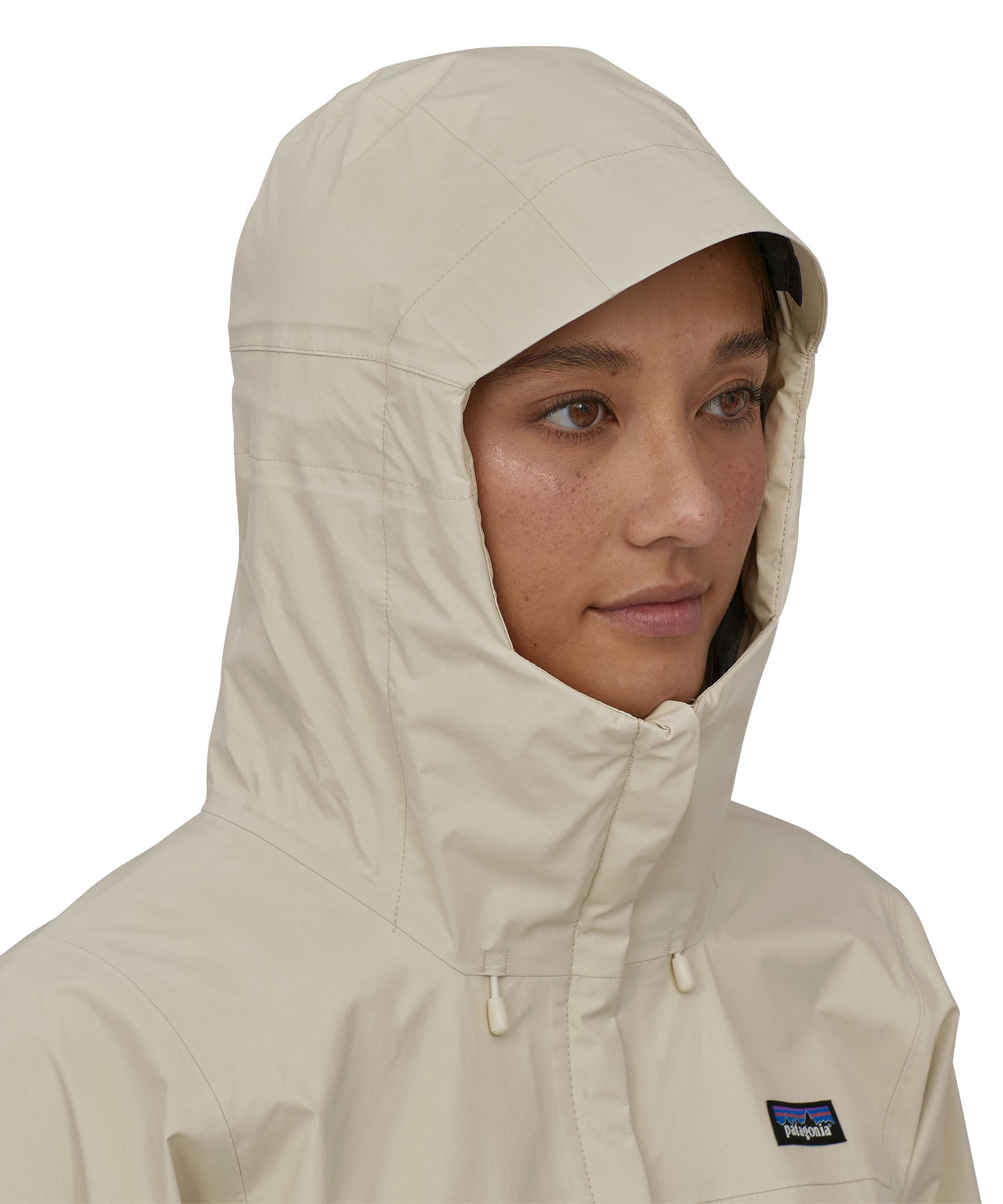 A person is wearing the Patagonia Women's Torrentshell 3L Rain Jacket and has the jacket fully zipped up with the hood up. The image is showing the coat zips all the way up to the chin and the hood comes quite far down to protect the face and neck from rain