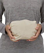 A person holding the Patagonia Women's Torrentshell 3L Rain Jacket whilst its in its storage bag. The coat is able to fit in two hands and is compact when stored in the bag