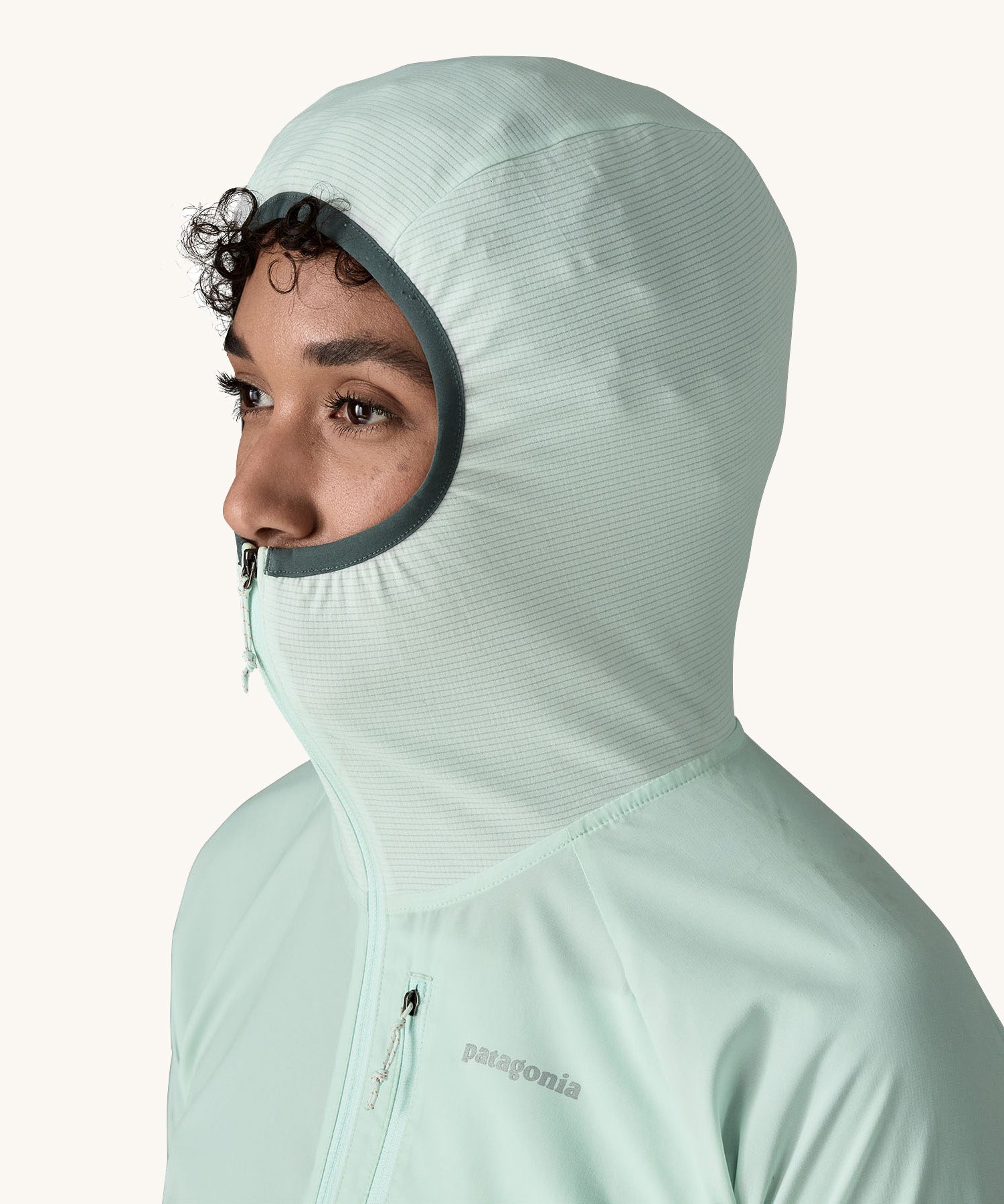 A close up of a female wearing the Patagonia lightweight jacket in light turquoise with the stretchy hood up and zip fully fastened 