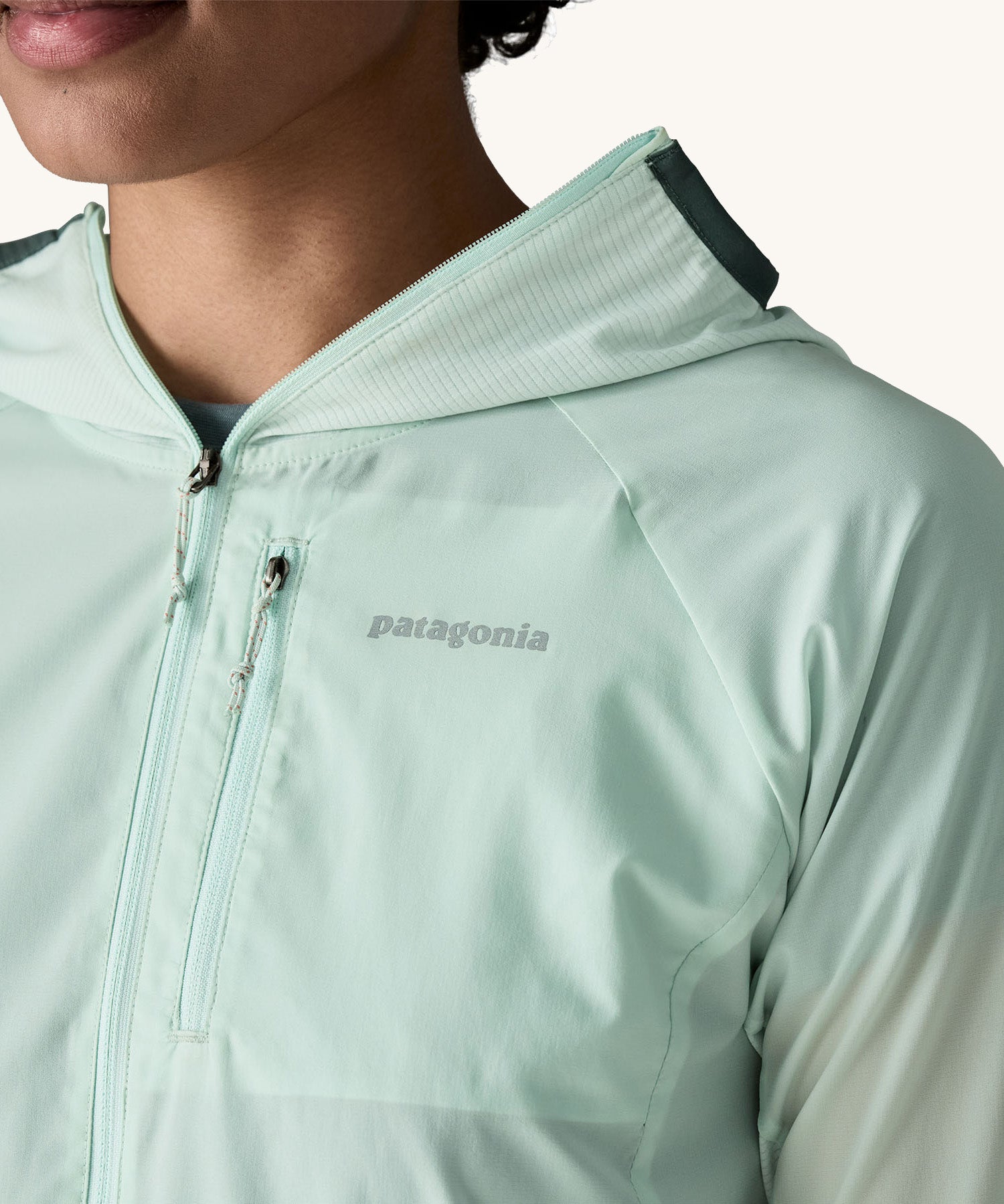 A close up of a female wearing the Patagonia lightweight jacket in light turquoise showing the zipped chest pocket