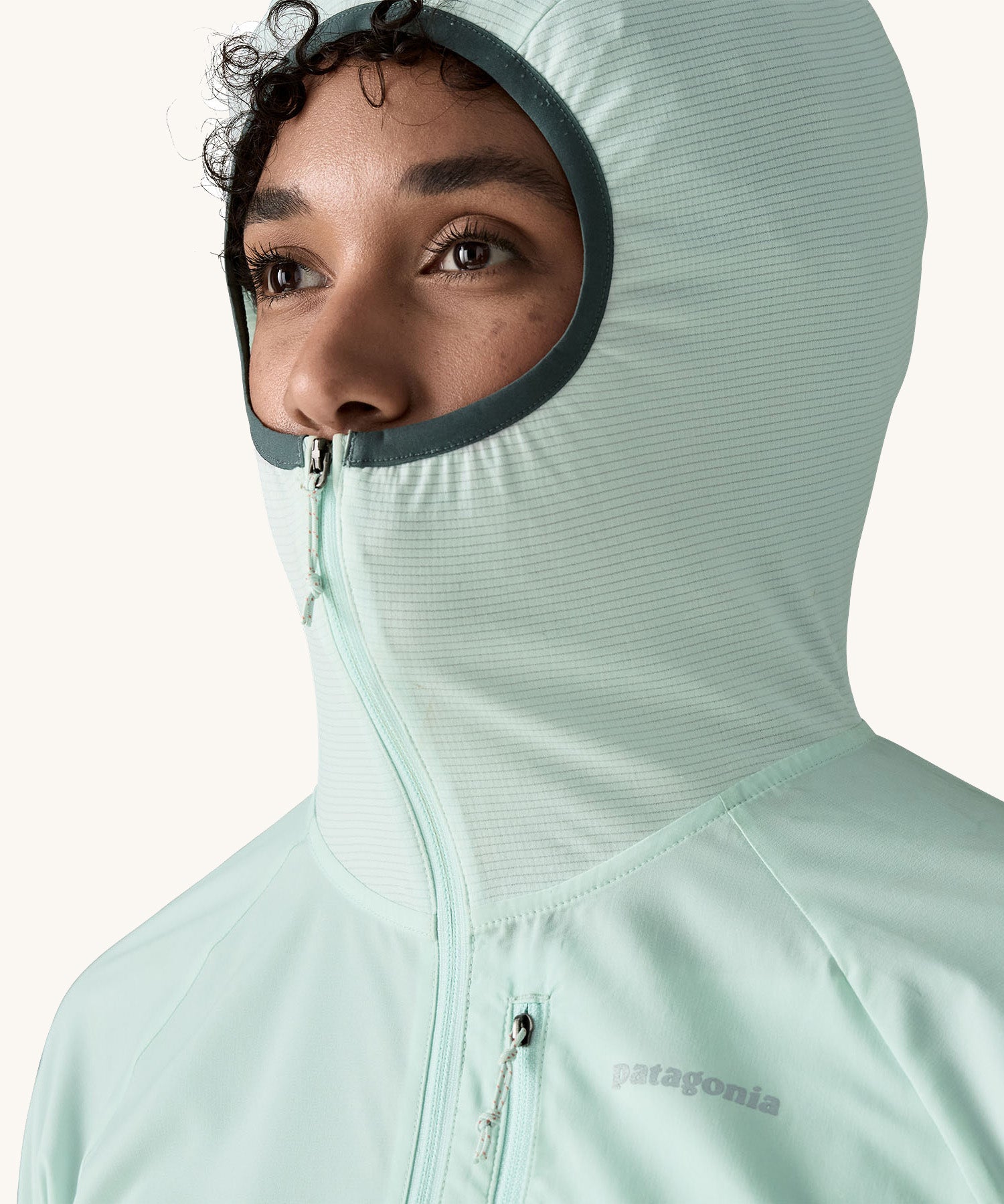 A close up of a female wearing the Patagonia lightweight jacket in light turquoise with the hood up and zip fully fastened 