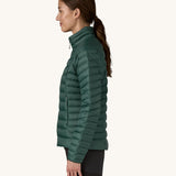 The side of the female standing in front of a cream background and wearing black trousers with the Patagonia puffer jacket in dark green with the zip fully fastened