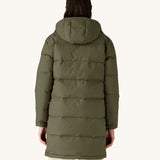 The back of the female model standing in front of a cream background and wearing the Patagonia dark green hooded parka jacket 