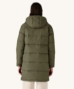 The back of the female model standing in front of a cream background and wearing the Patagonia dark green hooded parka jacket 