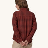 The back of the Female standing in front of a cream background and wearing cream corduroy trousers and the Patagonia brushed cotton shirt in red with a dark red check design.