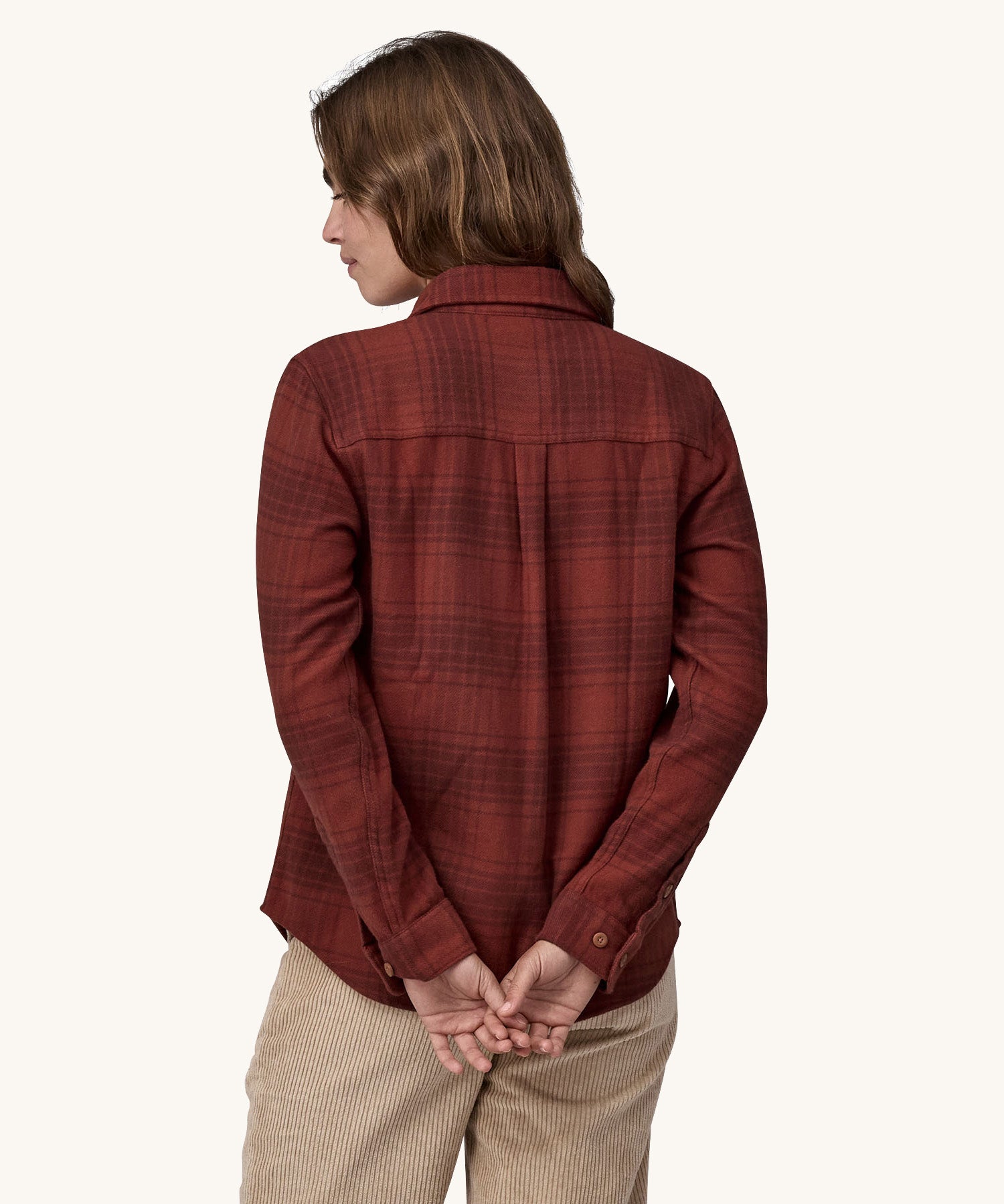 The back of the Female standing in front of a cream background and wearing cream corduroy trousers and the Patagonia brushed cotton shirt in red with a dark red check design.