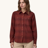 Female standing in front of a cream background and wearing cream corduroy trousers and the Patagonia brushed cotton buttoned shirt in red with a dark red check design.