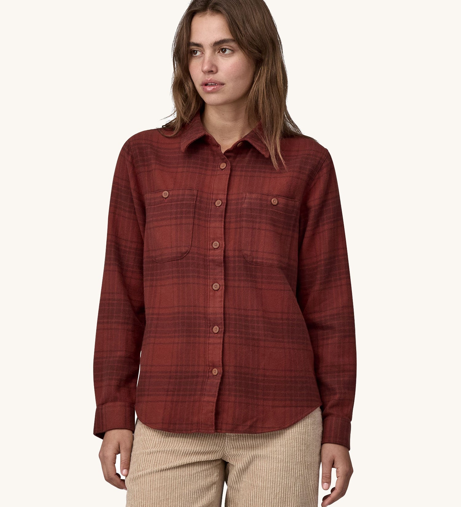 Female standing in front of a cream background and wearing cream corduroy trousers and the Patagonia brushed cotton buttoned shirt in red with a dark red check design.