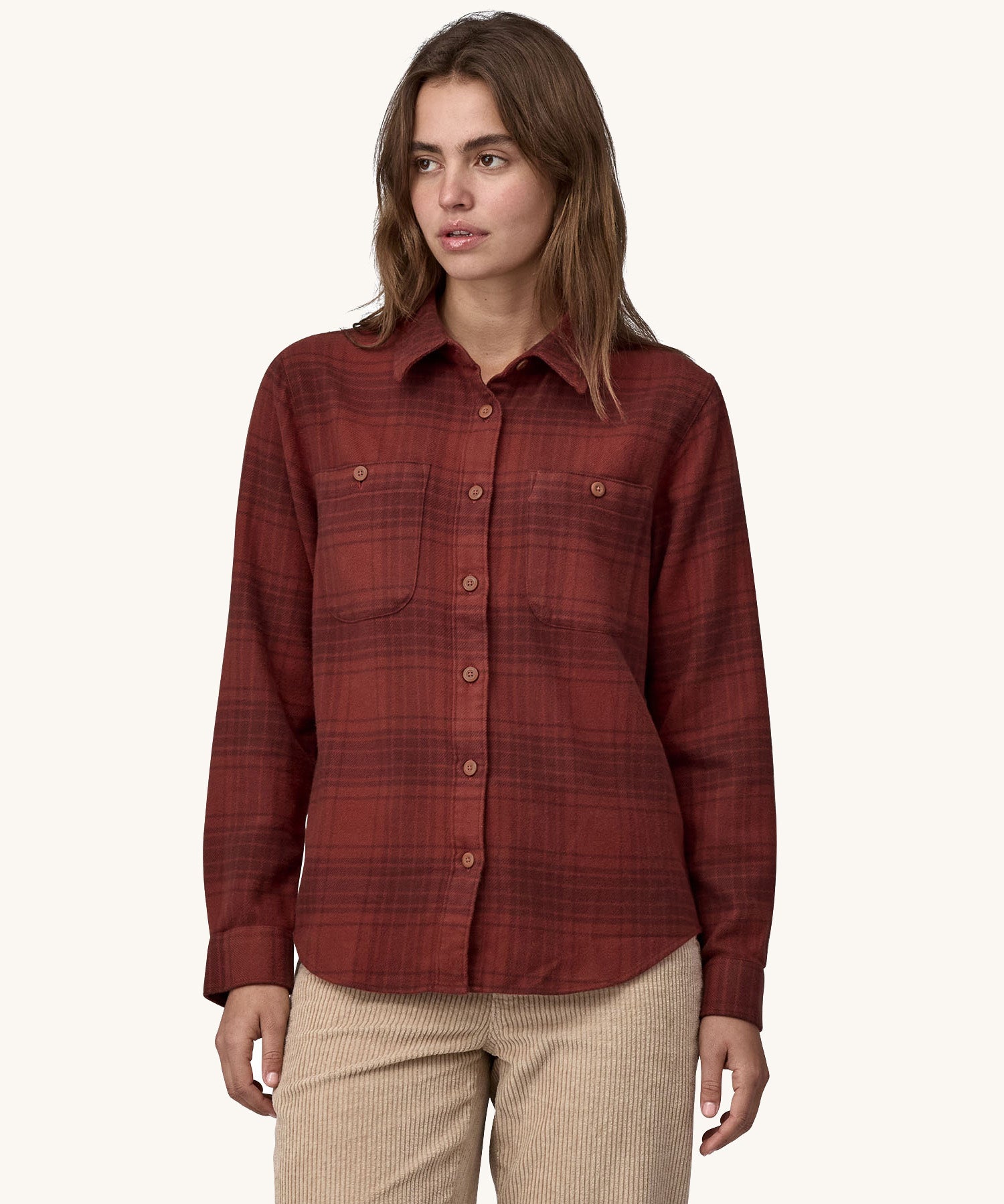 Female standing in front of a cream background and wearing cream corduroy trousers and the Patagonia brushed cotton buttoned shirt in red with a dark red check design.
