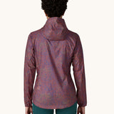 The back of a female standing in front of a cream background wearing dark green leggings and the Patagonia women's lightweight hooded rain jacket in dark red with a repeating purple pattern and the hood down