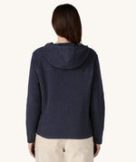 The back of the female standing in front of a cream background and wearing the dark blue Patagonia thick fleece with the hood down
