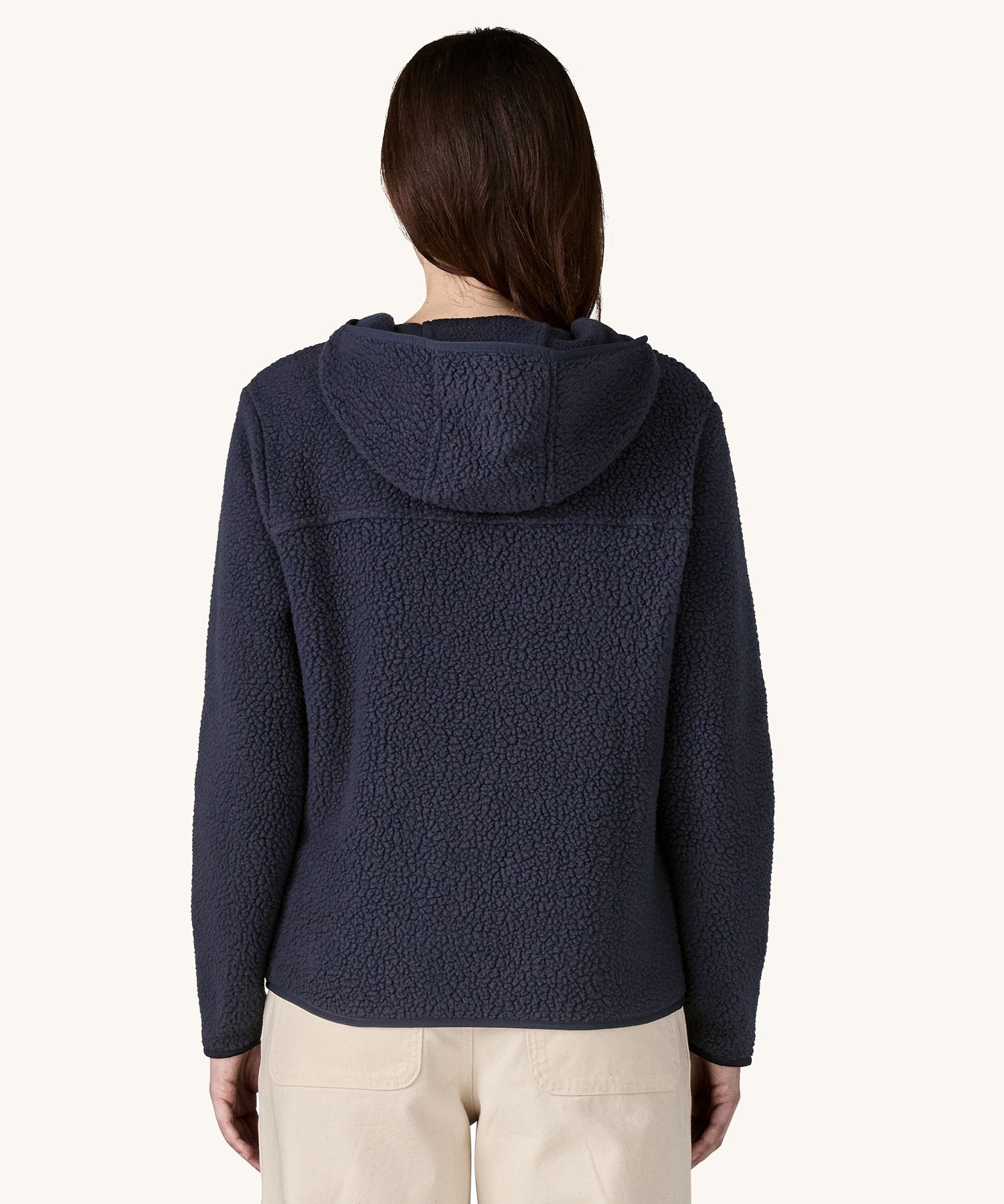 The back of the female standing in front of a cream background and wearing the dark blue Patagonia thick fleece with the hood down