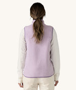 The back of the female standing in front of a cream background and wearing the light purple Patagonia women's thick fleece gilet 