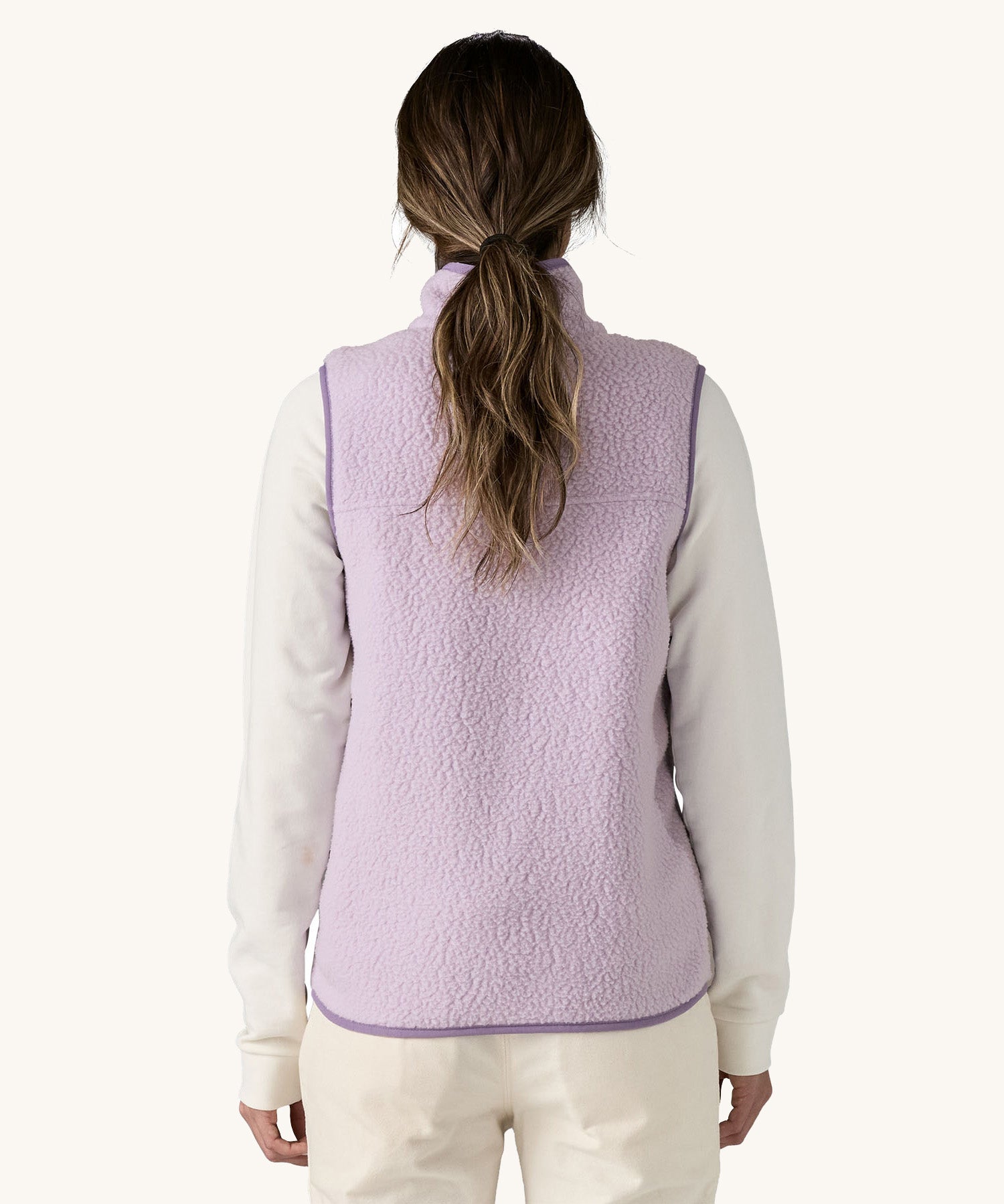 The back of the female standing in front of a cream background and wearing the light purple Patagonia women's thick fleece gilet 