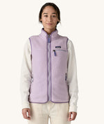 A female standing in front of a cream background and wearing the light purple Patagonia women's thick fleece gilet with the zip fully closed
