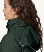 A close up of a female wearing the Patagonia women's parka coat in dark green with the zip full fastened and the hood down