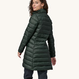The back of  female standing in front of a cream background, wearing dark blue jeans and the dark green puffer style that can be attached to the Patagonia green women's parka jacket with the zip fastened