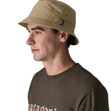 Man wearing Patagonia's 100% recycled nylon water repellent adult bucket hat in light brown. Shows 2 air holes on the side