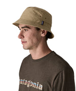 Man wearing Patagonia's 100% recycled nylon water repellent adult bucket hat in light brown. Shows 2 air holes on the side