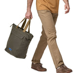 A person carrying the Patagonia Waxed Canvas Tote Pack Basin Green, in their hand using the carry straps