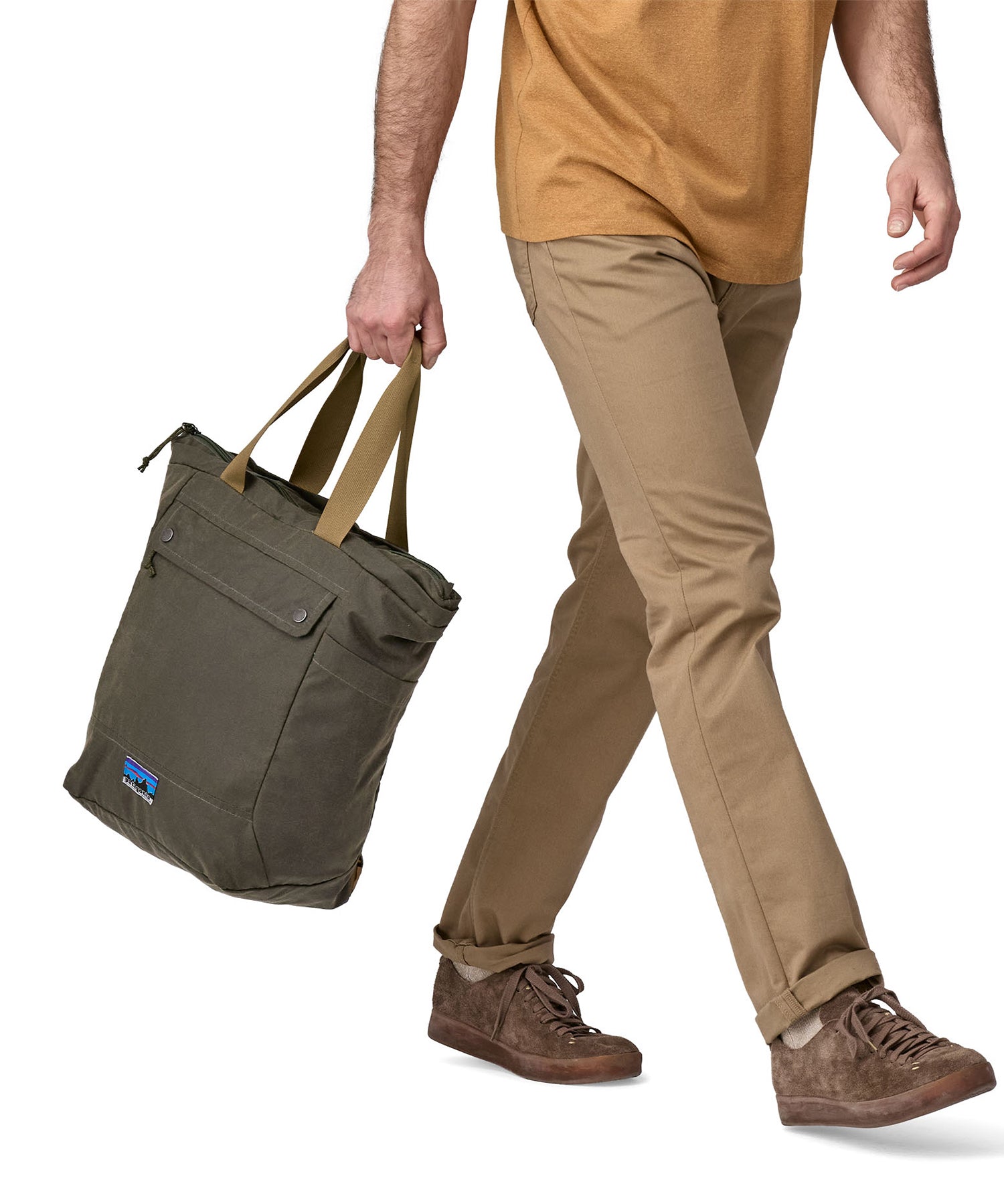 A person carrying the Patagonia Waxed Canvas Tote Pack Basin Green, in their hand using the carry straps