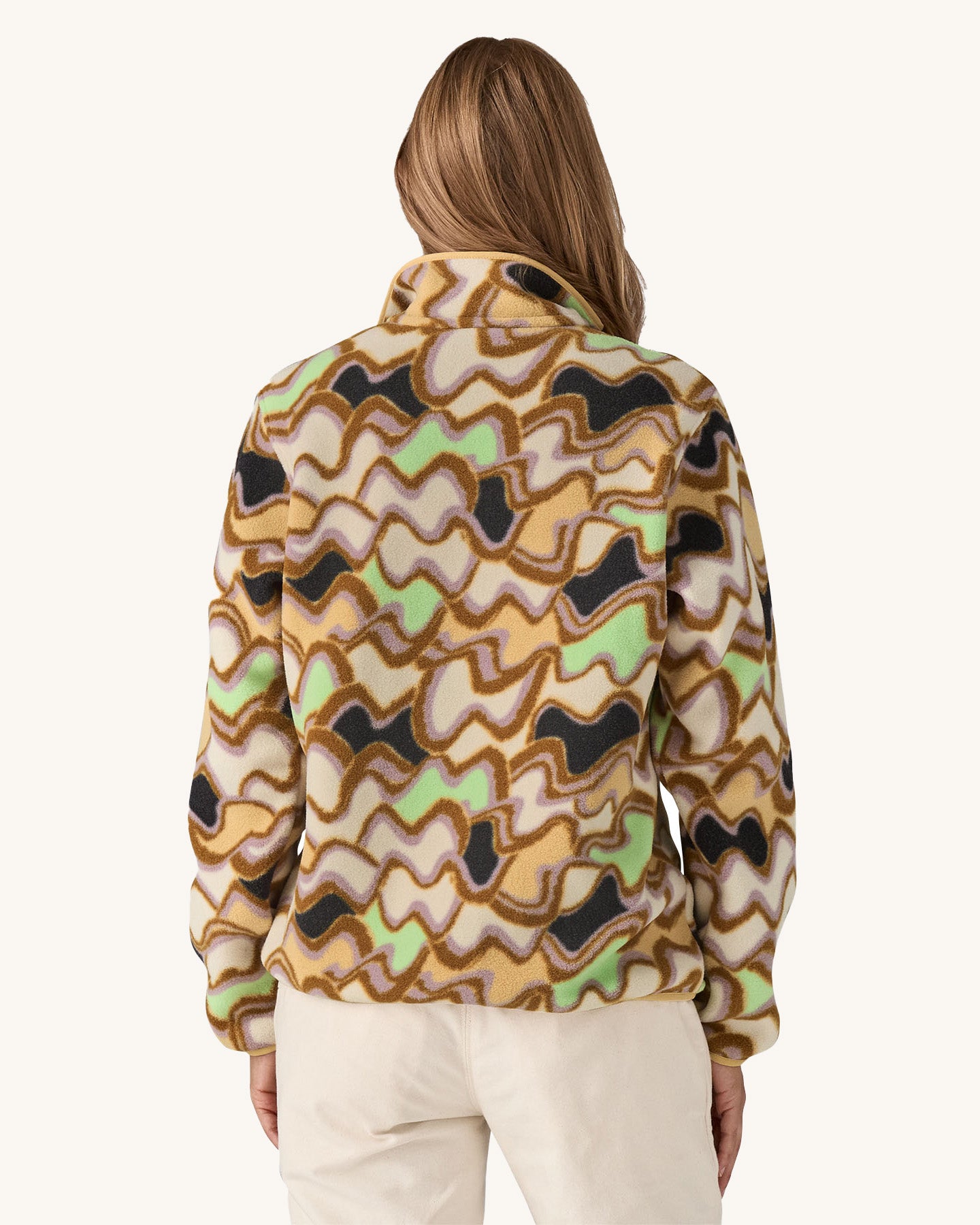 Patagonia Women’s Lightweight Synchilla Snap-T Fleece in Small Currents shown on a woman; beige fleece with pastel wave pattern in purple, green, and brown, plus a breast pocket and snap-button collar. Available at Babipur.