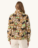 Patagonia Women’s Lightweight Synchilla Snap-T Fleece in Small Currents shown on a woman; beige fleece with pastel wave pattern in purple, green, and brown, plus a breast pocket and snap-button collar. Available at Babipur.