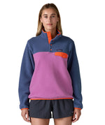 A woman wearing the Patagonia synchilla jacket in brisk purple available at Babipur. A pale purple and pink fleece type jacket with orange trim details. Features the logo patch stitched on the left chest pocket, popper fasteners and a chest pocket. 