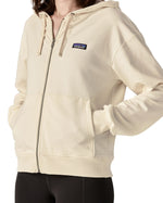 Close up of Woman wearing Patagonia's women's full zip Anhya hoody in cream with hands in the pouch pockets