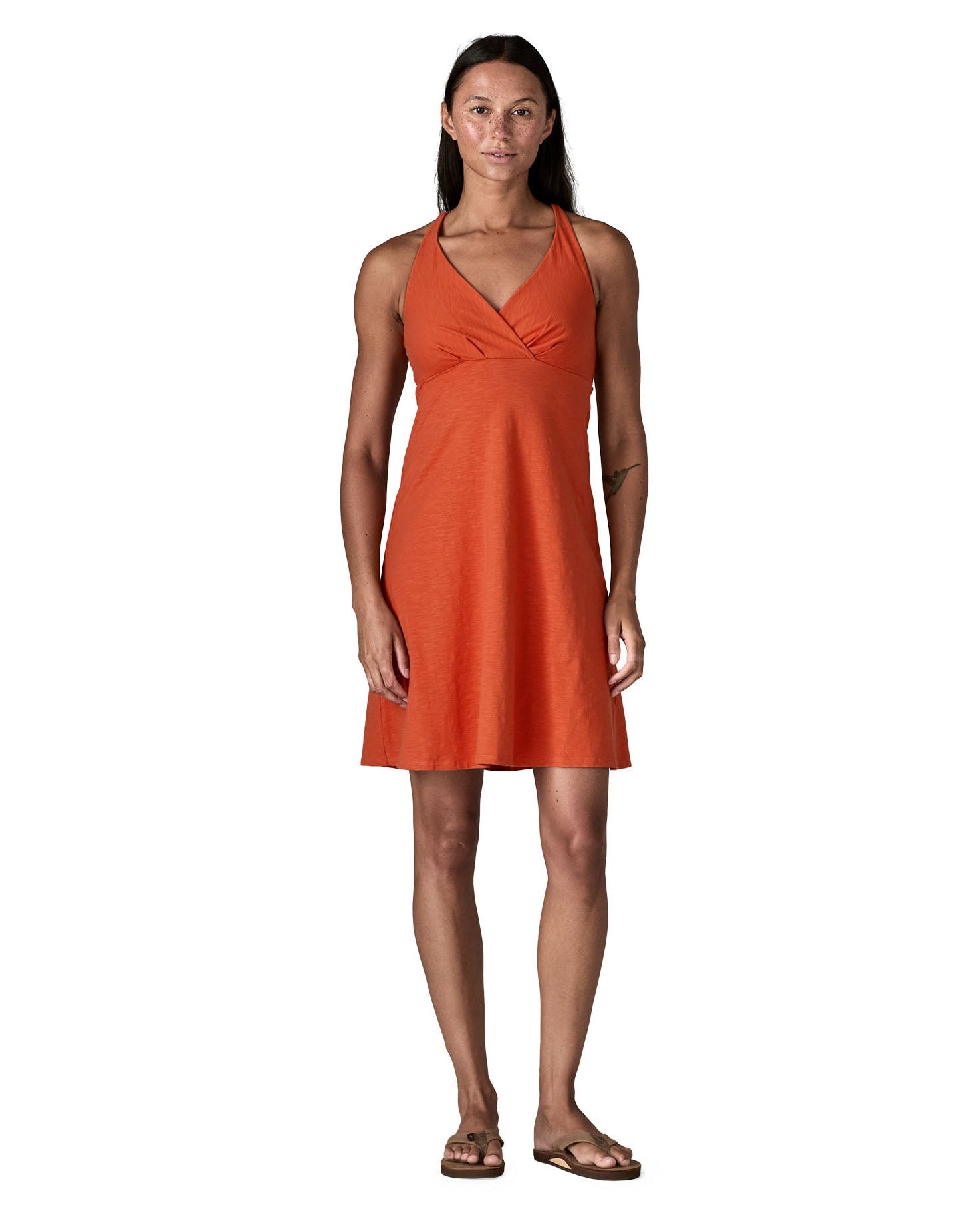 Woman wearing Patagonia's amber dawn sleeveless dress in orange.  Dress  has front low v neck and knee-height
