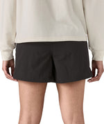 Back of woman wearing Patagonia's quick drying women's baggies shorts in black. Shorts have a loose fit