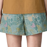 Back of Side of woman wearing Patagonia's women's baggies shorts in black with repeating abstract design. Shorts have a loose fit
