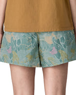 Back of Side of woman wearing Patagonia's women's baggies shorts in black with repeating abstract design. Shorts have a loose fit