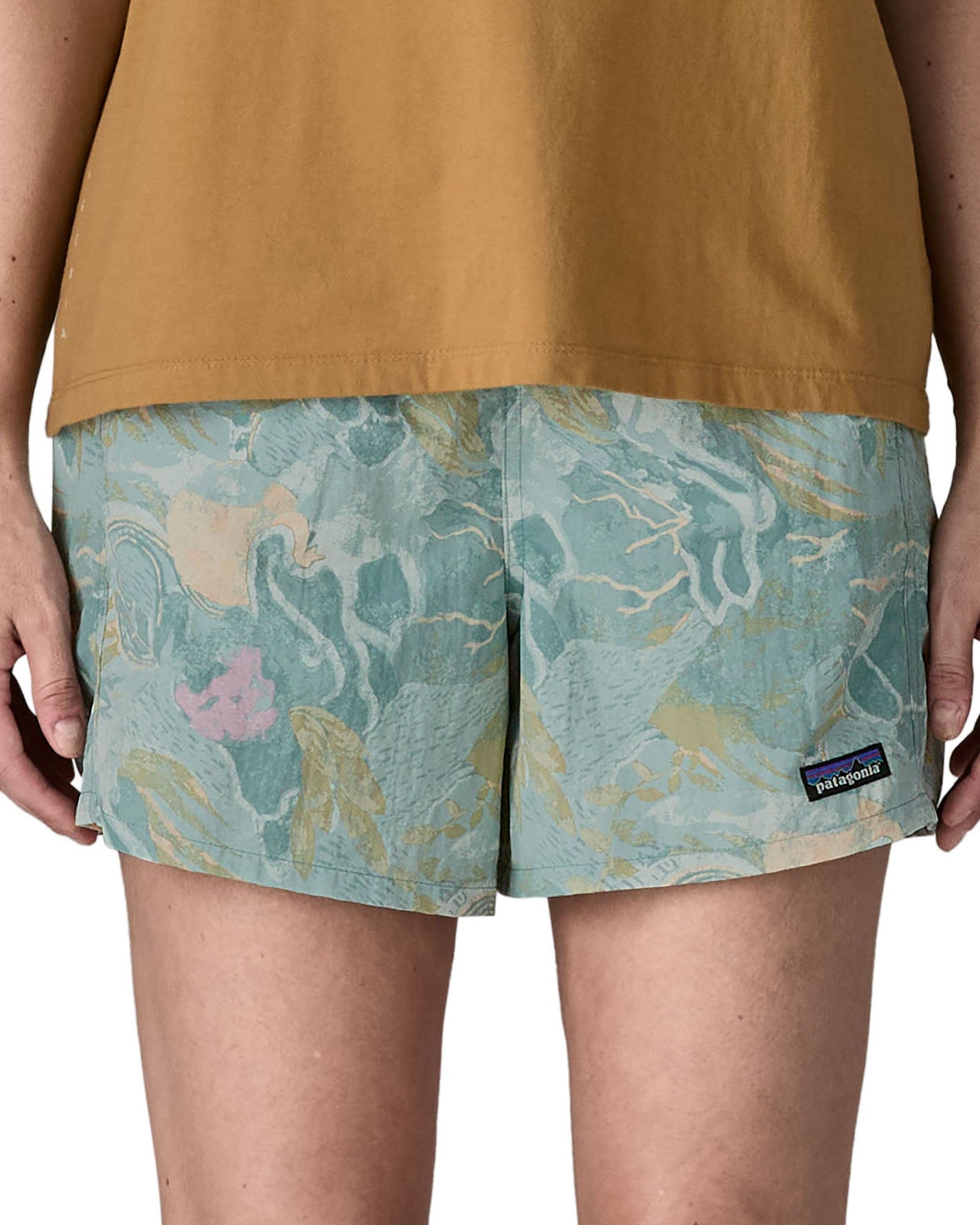 Woman wearing Patagonia quick drying women's baggies shorts in light blue with repeating abstract design. Shorts have a loose fit