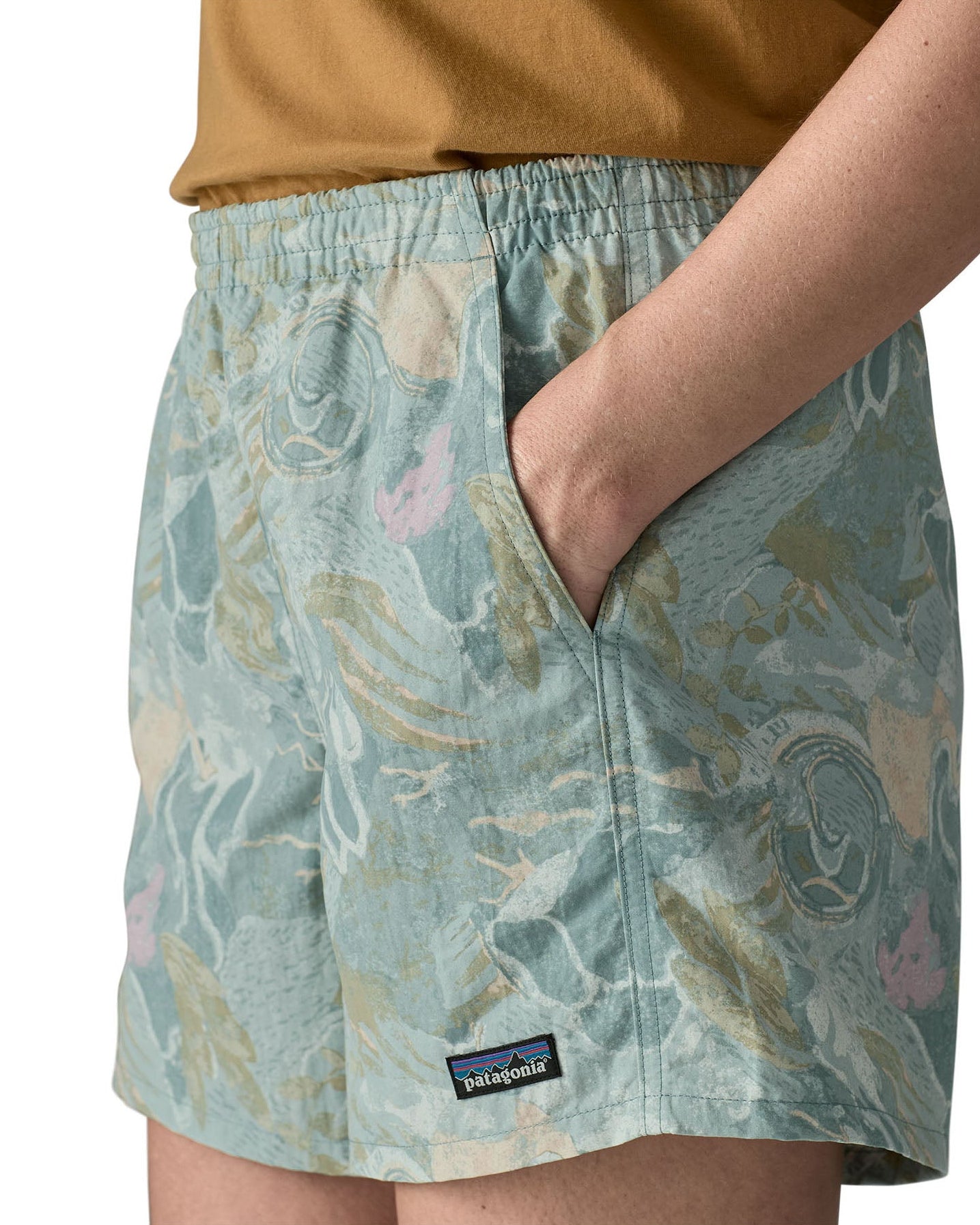 Side of woman wearing Patagonia quick drying women's baggies shorts in light blue with repeating abstract design with hand in pocket
