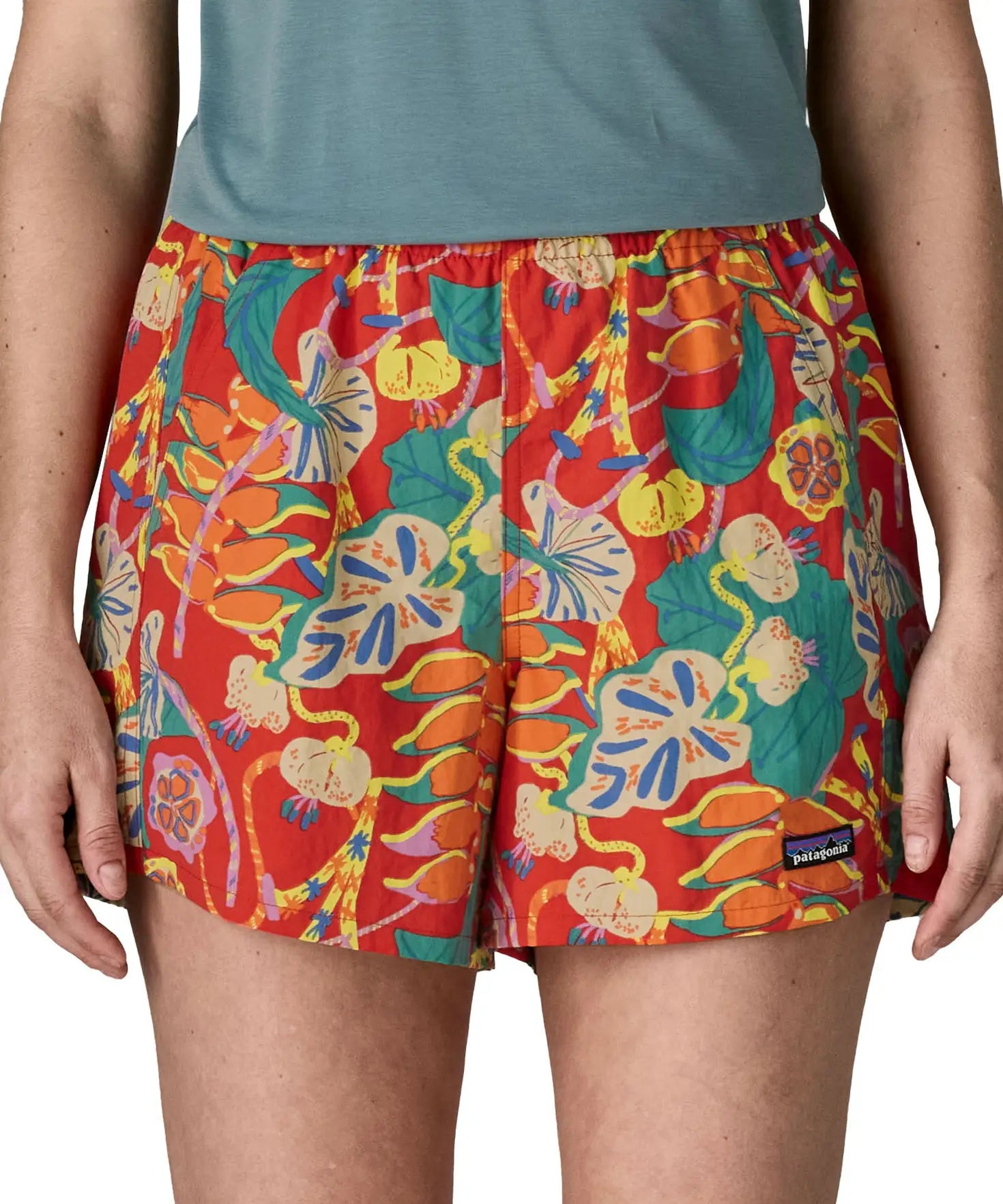 Woman wearing Patagonia quick drying women's baggies shorts in red with repeating abstract tropical design. Shorts have a loose fit