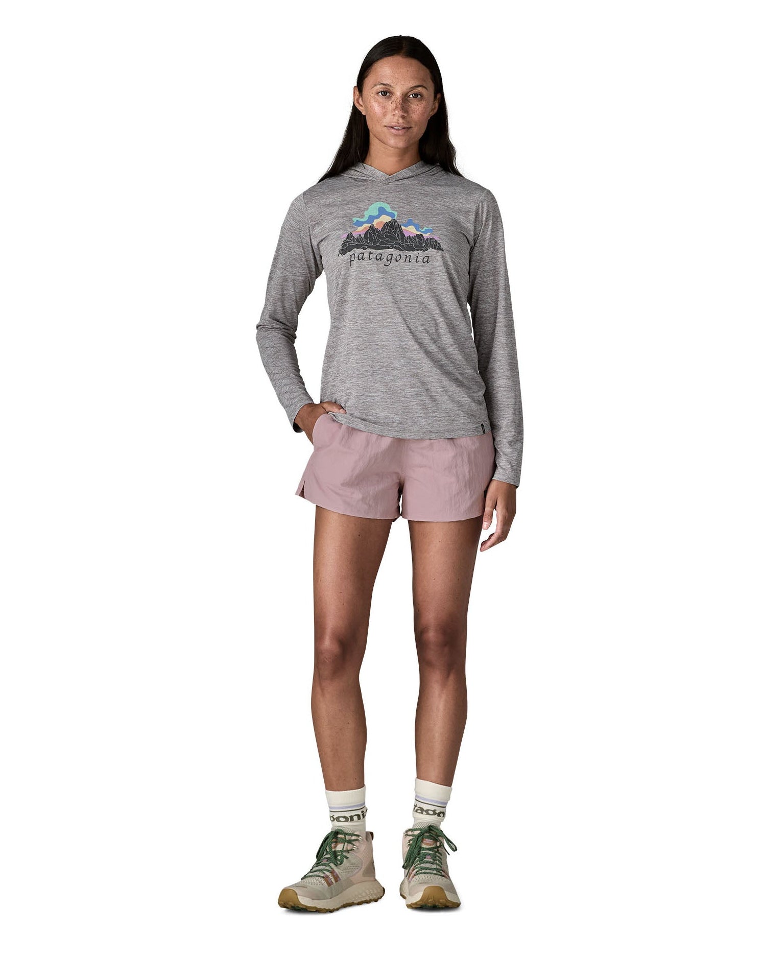 Woman wearing Patagonia's quick drying women's barely baggies shorts in light pink with hand in side pocket. 