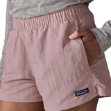 Woman wearing Patagonia's quick drying women's barely baggies shorts in light pink with hand in side pocket. Shorts have a loose fit