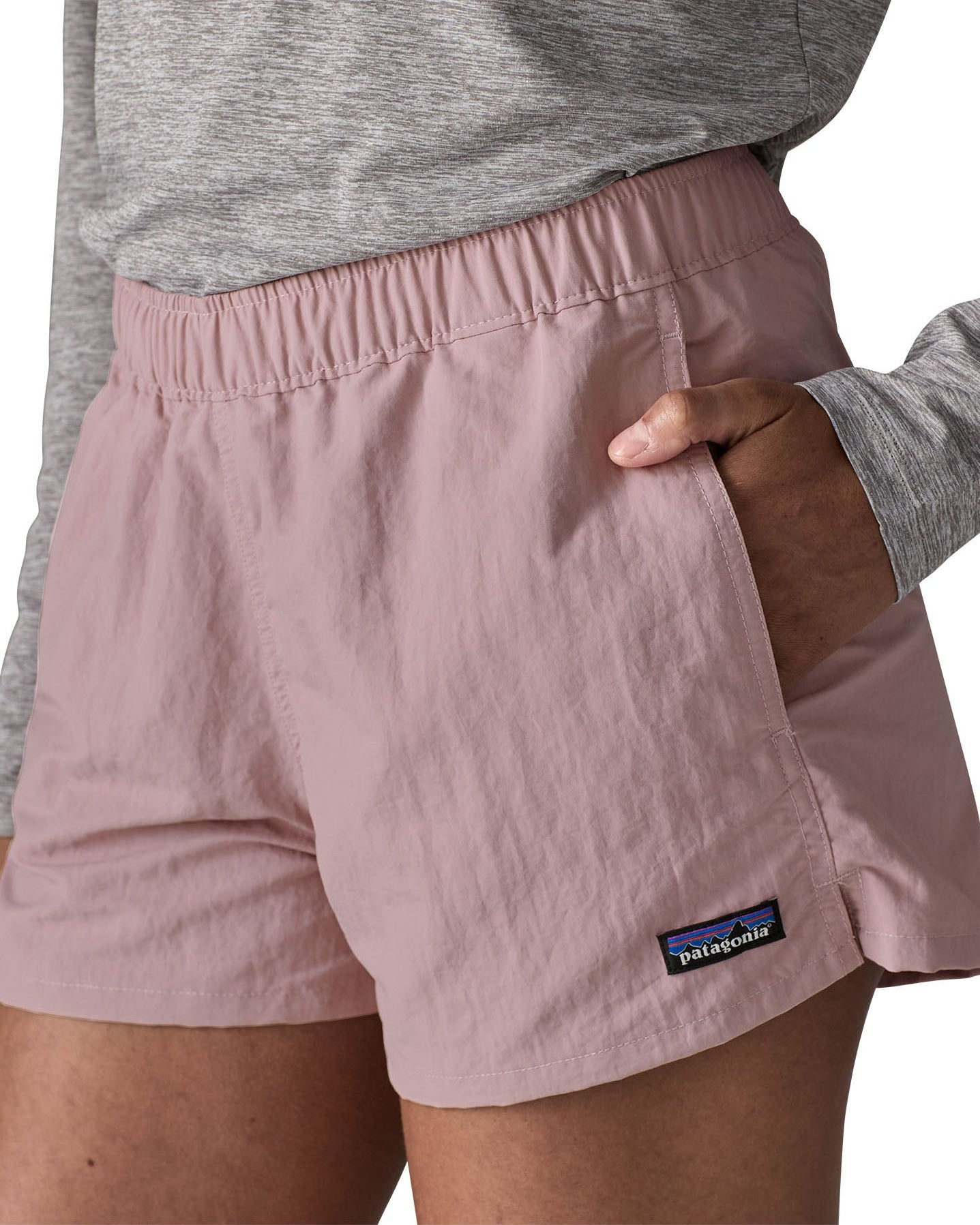 Woman wearing Patagonia's quick drying women's barely baggies shorts in light pink with hand in side pocket. Shorts have a loose fit