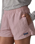 Woman wearing Patagonia's quick drying women's barely baggies shorts in light pink with hand in side pocket. Shorts have a loose fit