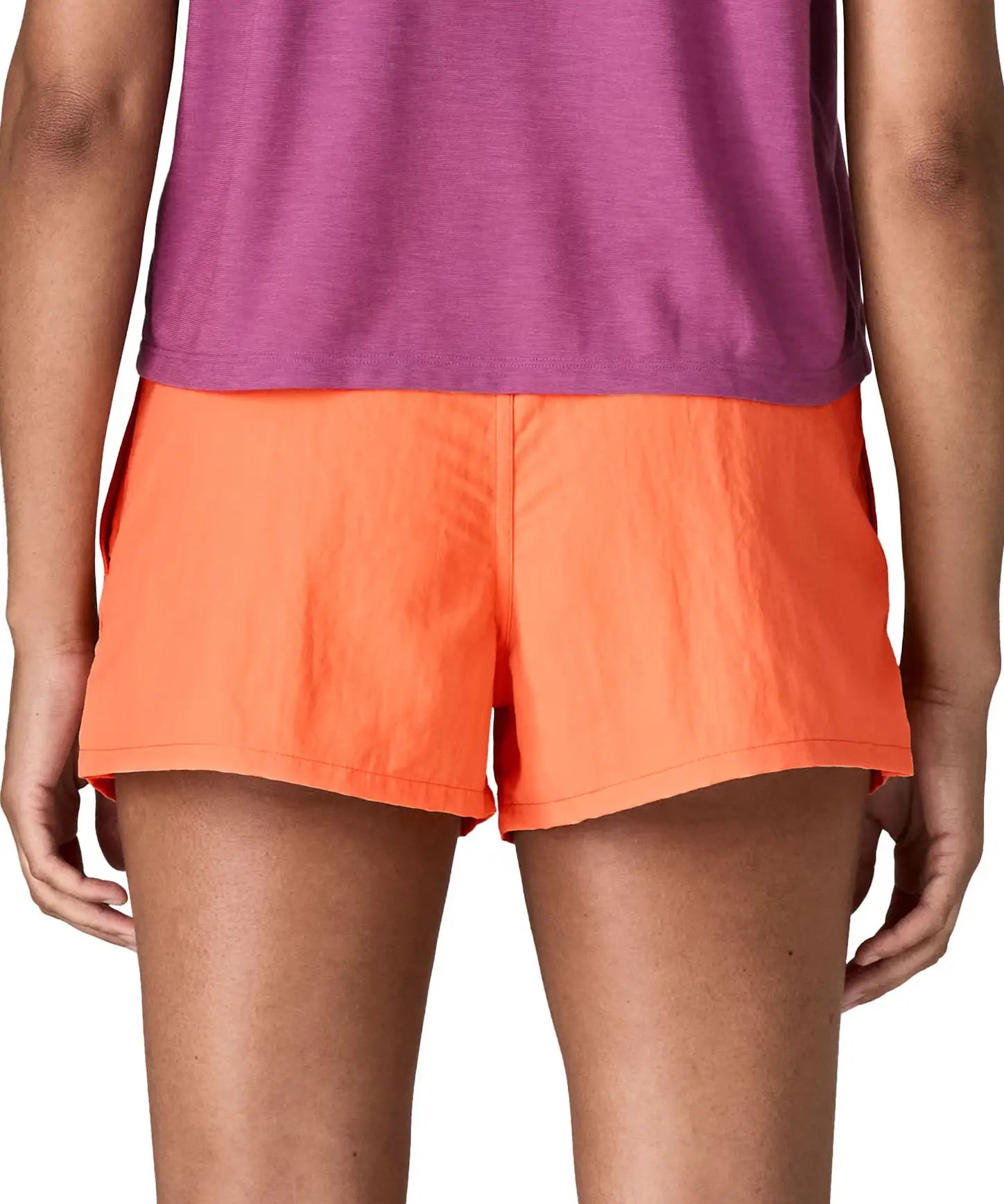 Back of woman wearing Patagonia's quick drying women's barely baggies shorts in bright orange. Shorts have a loose fit