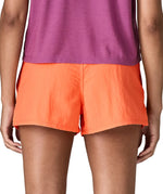 Back of woman wearing Patagonia's quick drying women's barely baggies shorts in bright orange. Shorts have a loose fit