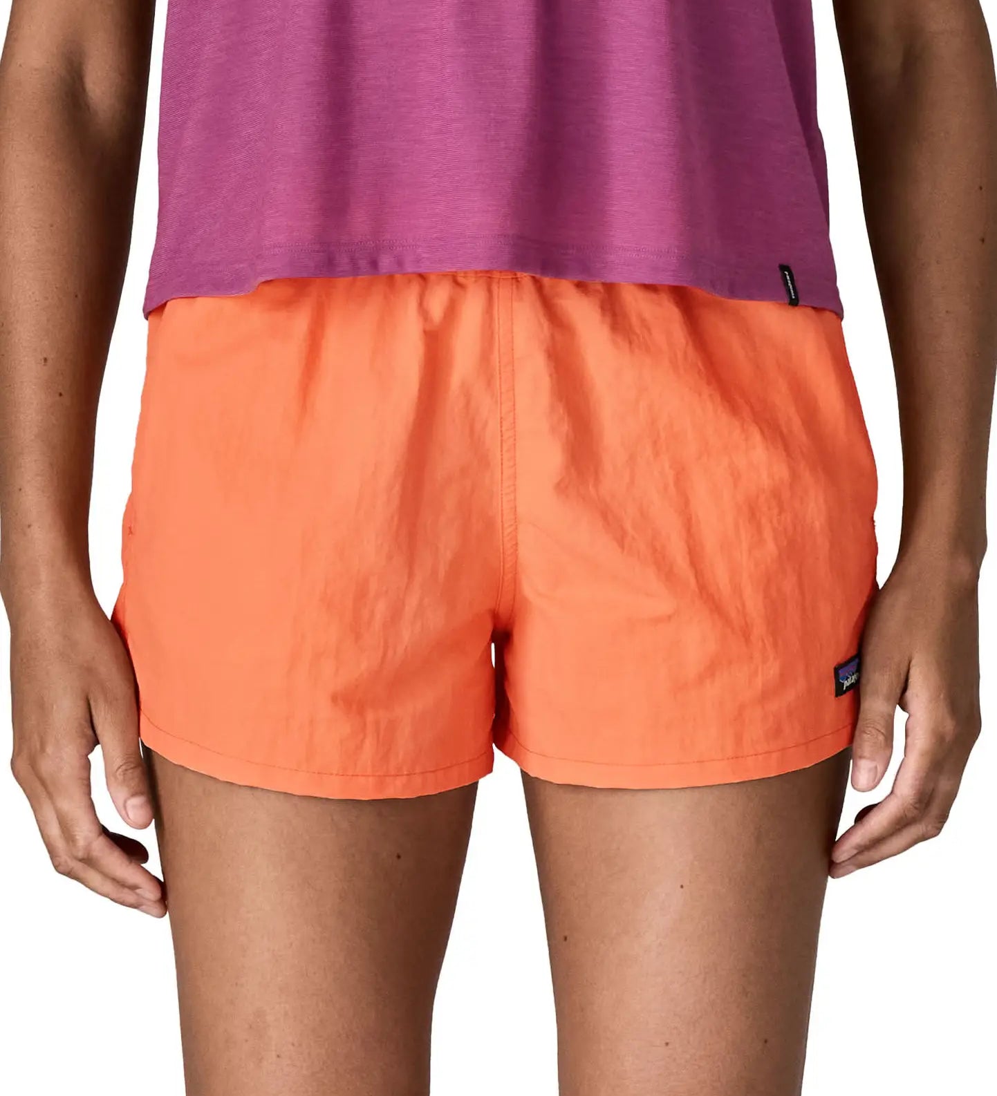 Front of woman wearing Patagonia's quick drying women's barely baggies shorts in bright orange. Shorts have a loose fit